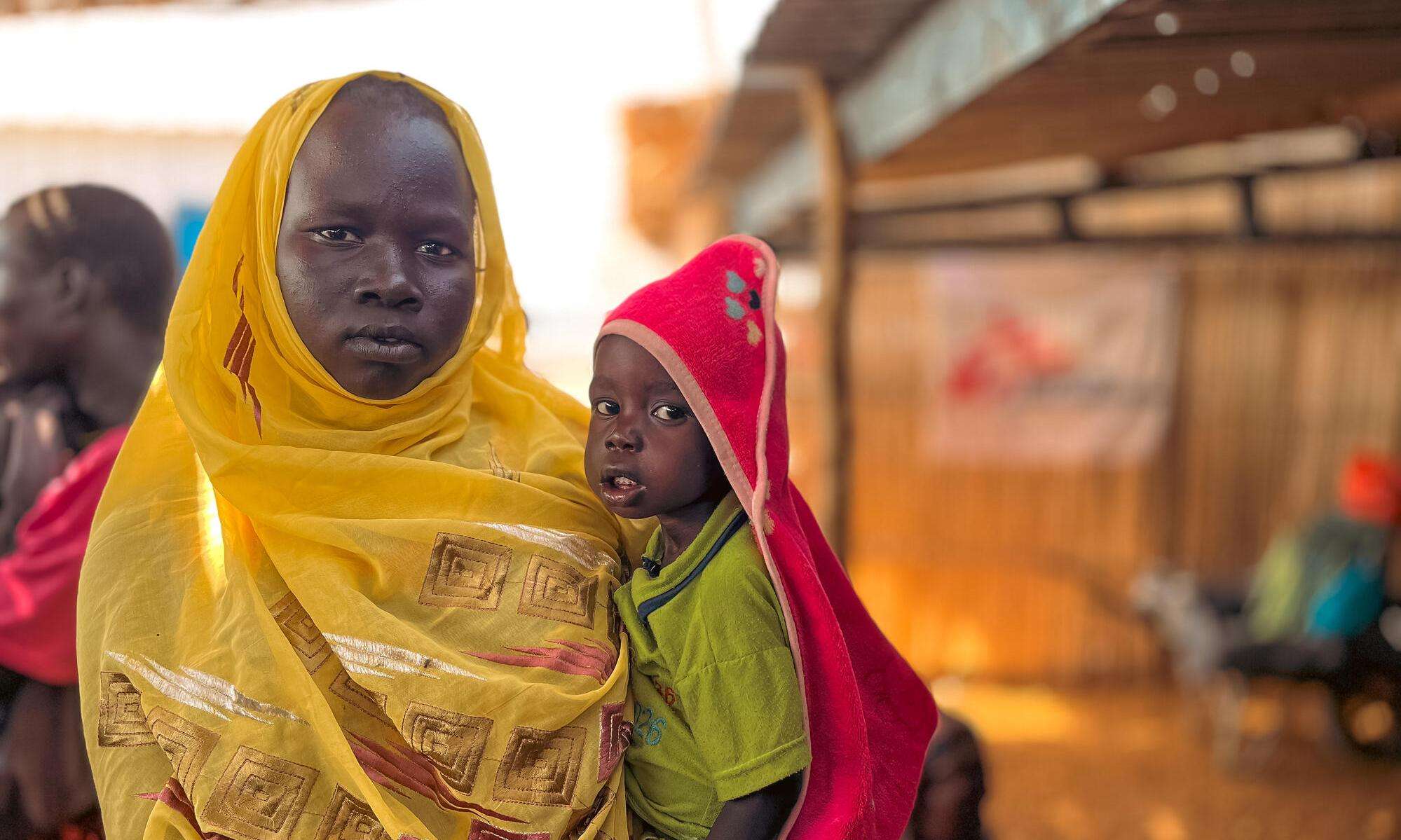 A woman in a yellow scarf and her child who are internally displaced in Sudan due to the current conflict.
