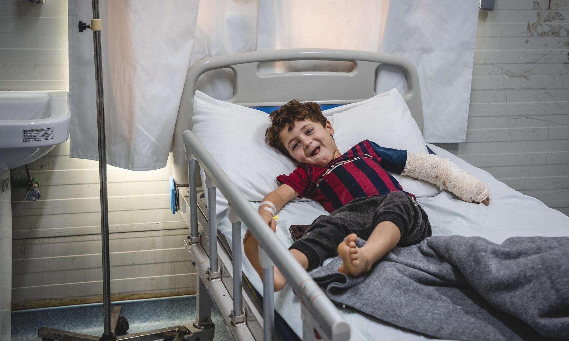 A smiling boy with an arm cast on a hospital bed in Mosul, Iraq.