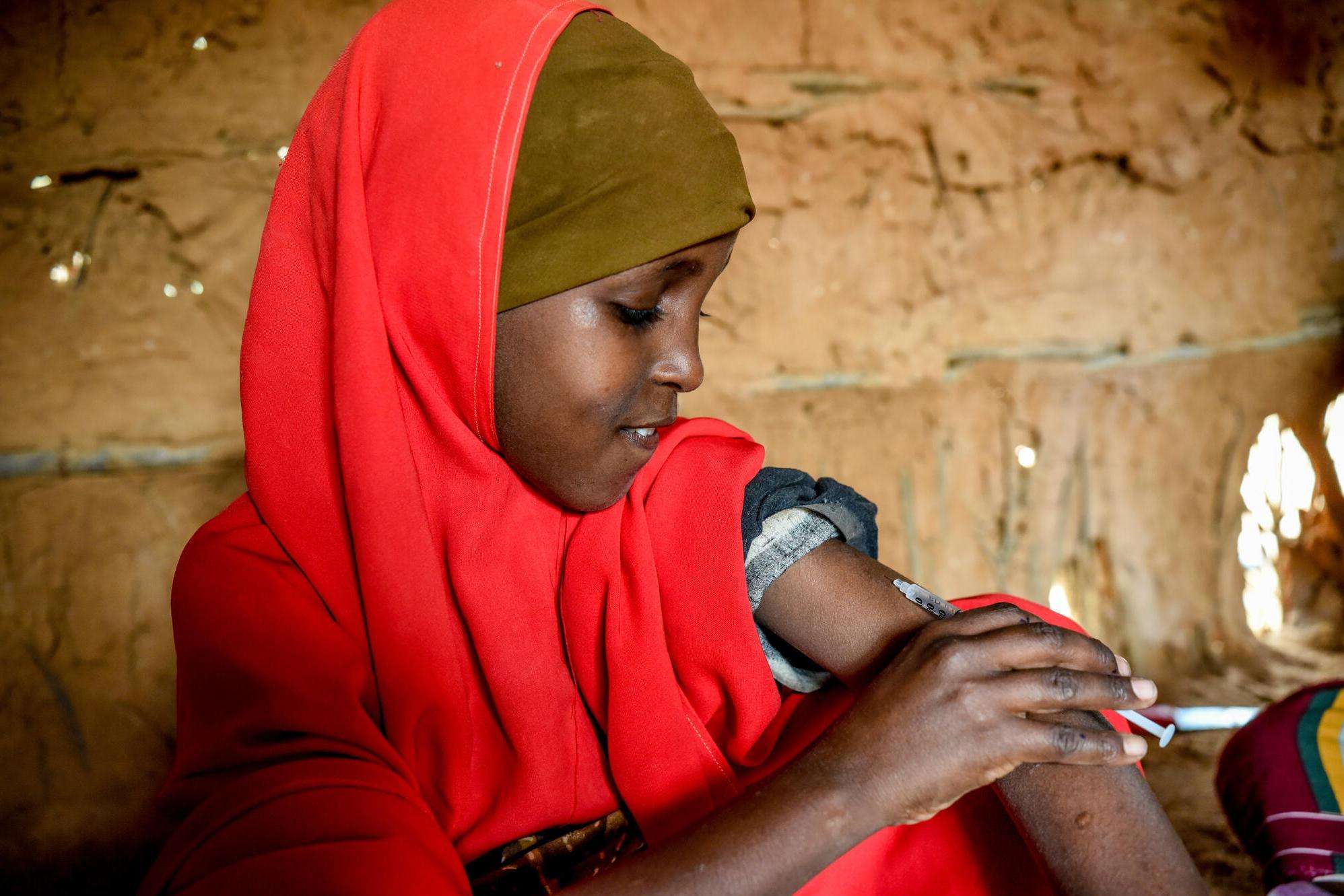 A young girl in a red headscarf injects insulin in Kenya.