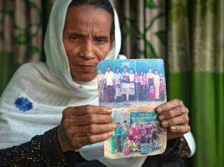 An older woman holds up two photographs of her family members.