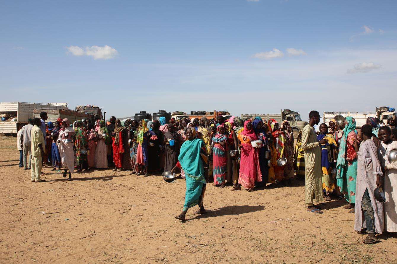A woman in turquoise dress walks in front of a crowd at a food distribution in Chad for Sudanese refugees
