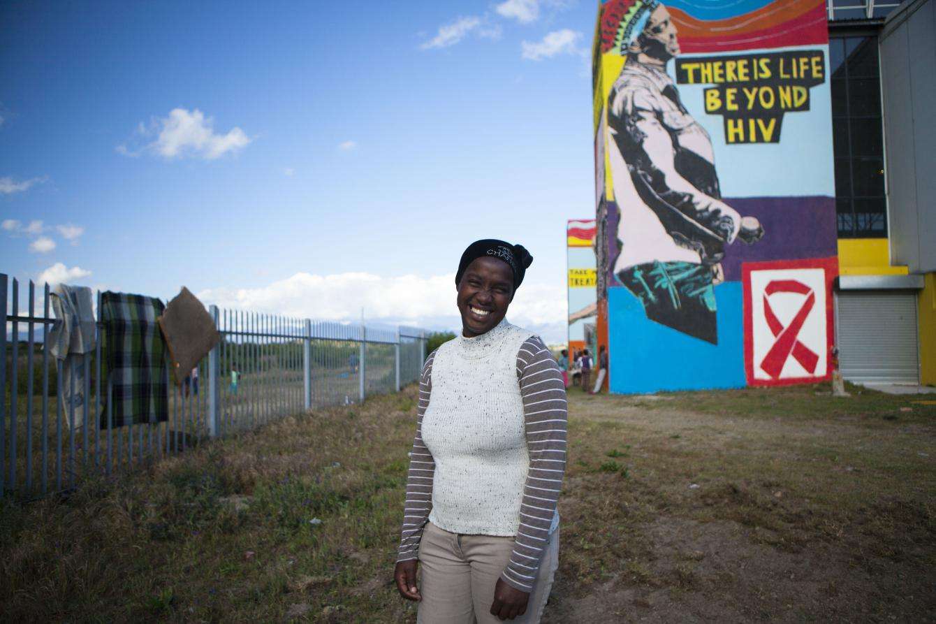 A woman smiling in a field in front of a mural about AIDS