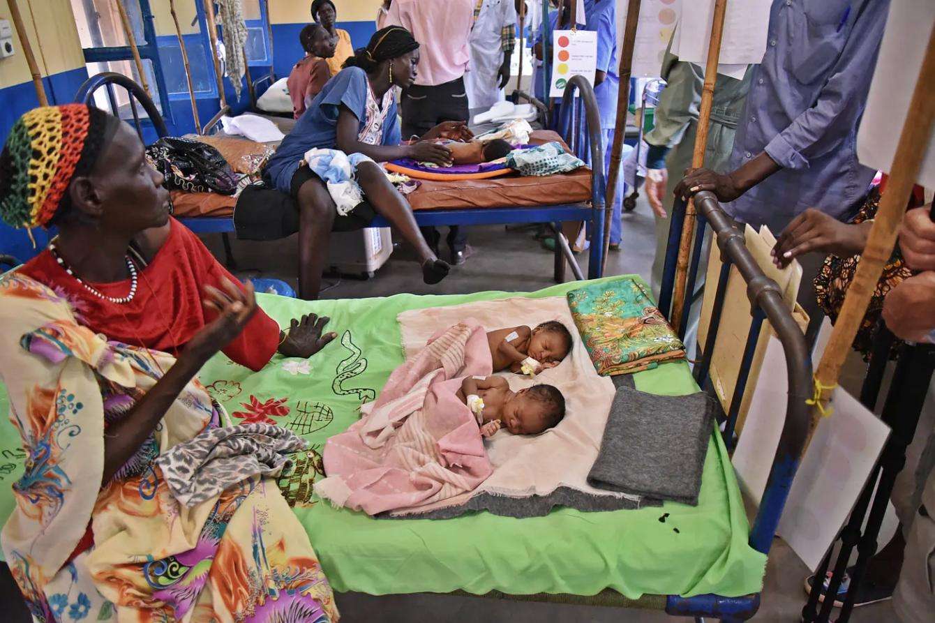 A woman with two babies on a bed in Aweil State Hospital in South Sudan.