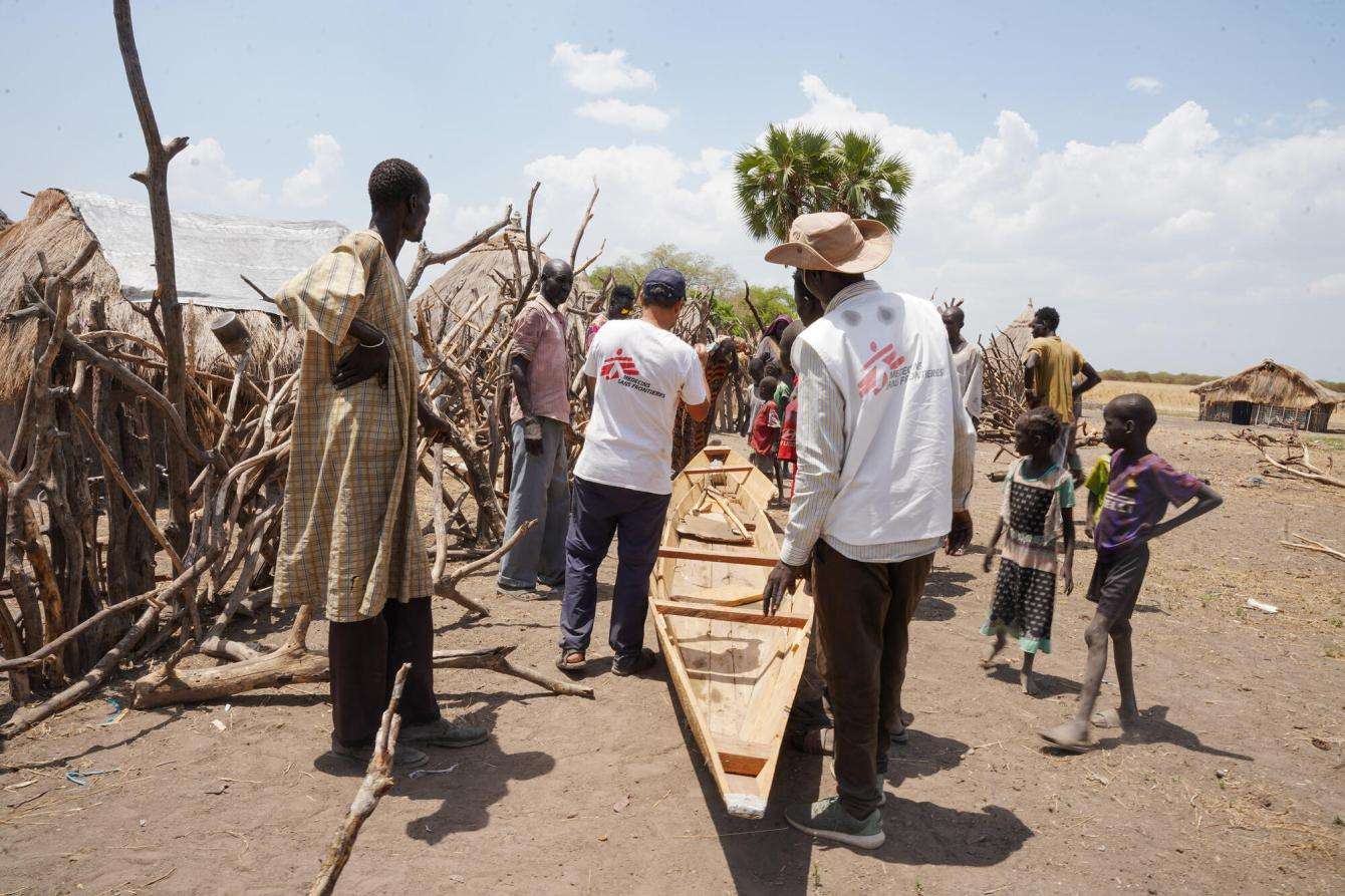 MSF staff in white vests and community members look at canoe donated for rainy season in South Sudan
