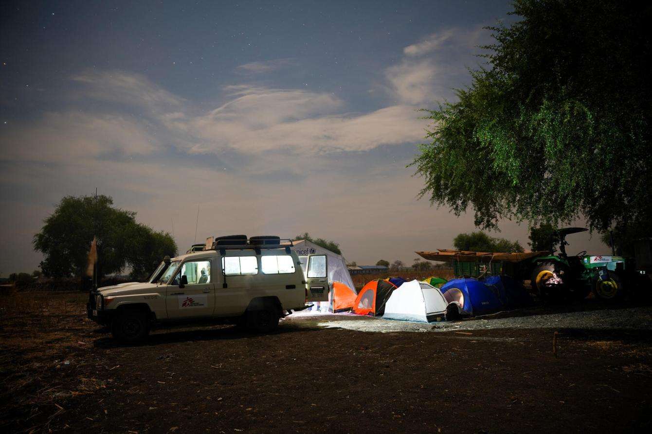 MSF vehicle parked in desert beside trees at night with windows alight. 