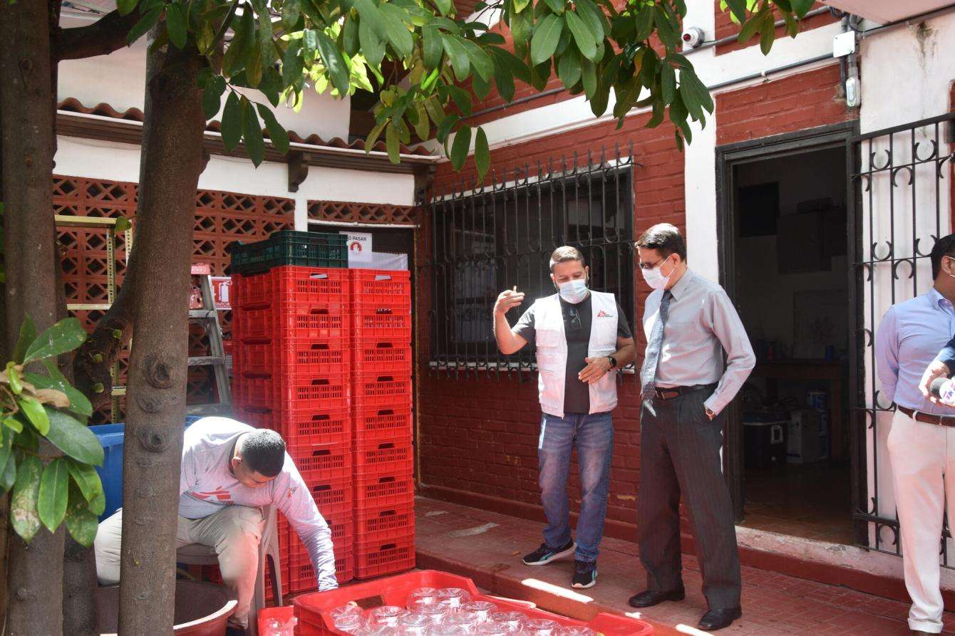 Two men stand outside looking at a stack of jars. 