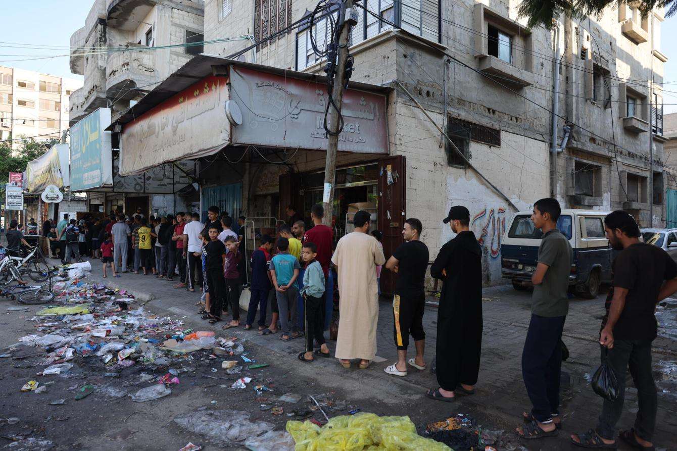 Palestinians line up on a rubble-strewn street in Gaza.