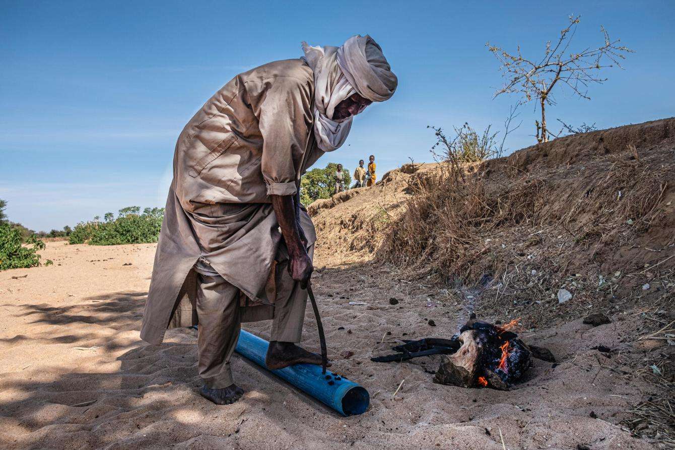 A man burns holes into a plastic pipe to collect water from a wadi in Chad.