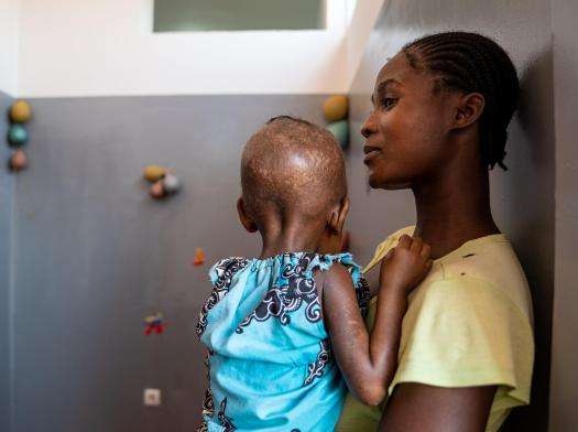 Young woman and daughter stand against lockers at a hospital in Angola