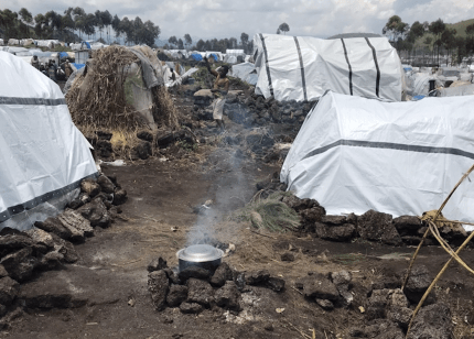A pot on a makeshift stove on the muddy ground in a displacement camp surrounded by tents near Goma, Democratic Republic of Congo