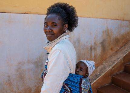 MSF community health worker smiles carrying child on back in Angola.