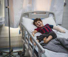 A smiling boy with an arm cast on a hospital bed in Mosul, Iraq.