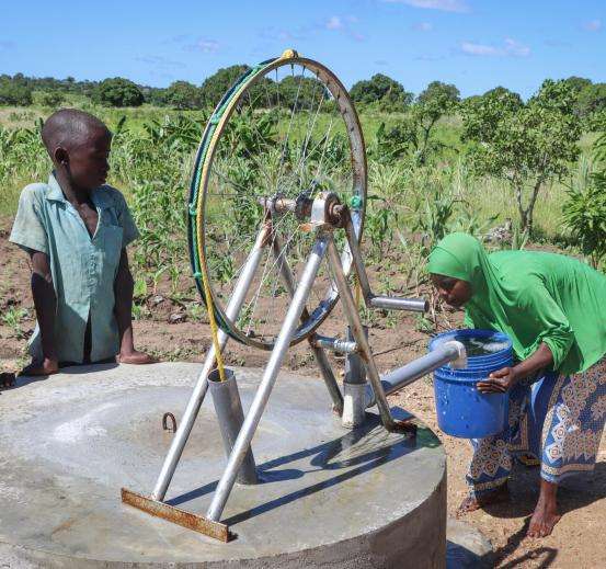 Community members use a bicycle gear to power water collection from a well. 