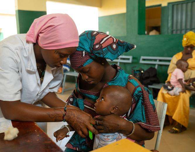 A mother holder her child while he is examined by a nurse in Niono, Mali 